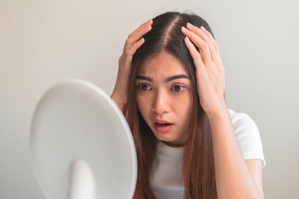 Woman looking at her scalp in the mirror with a shocked expression.