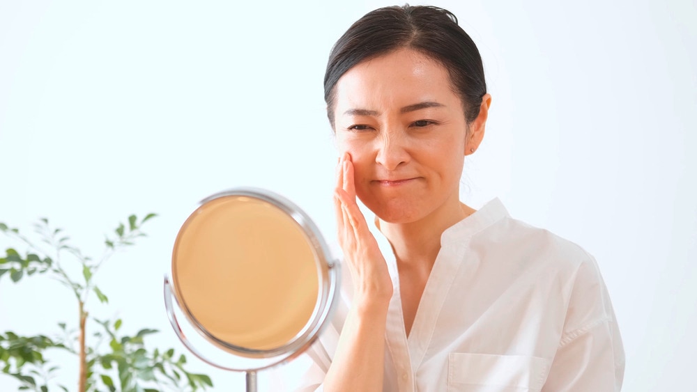 Woman touching her face while looking at her reflection in the mirror.