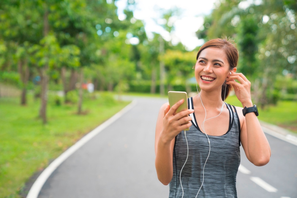 Asian woman wearing earphones while jogging outside