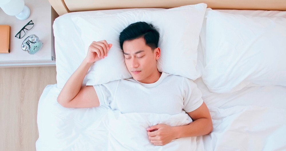 Asian man sleeping on fresh sheets.