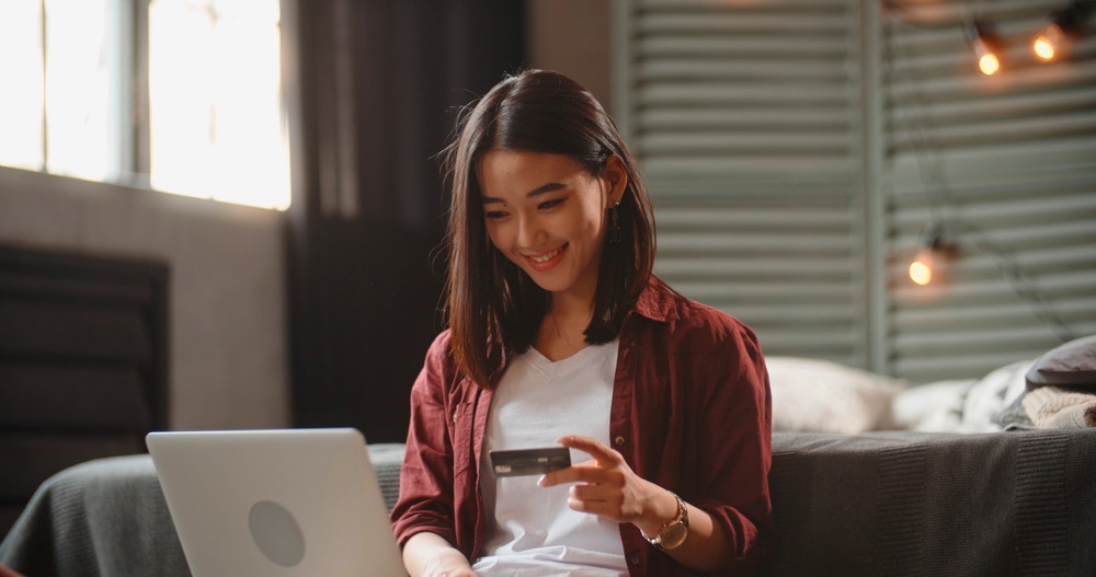 Asian woman holding a credit card while online shopping.