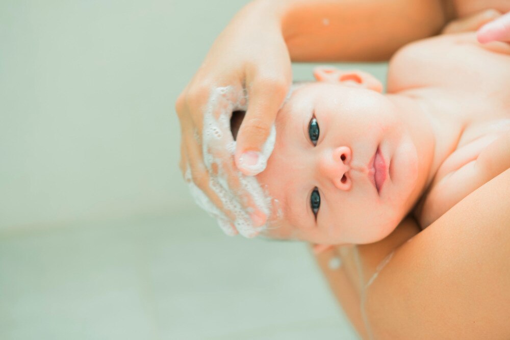 A portrait of mother shampooing her newborn’s hair. 