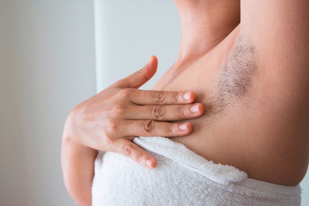 Woman wrapped in white towel touching her hairy underarms.