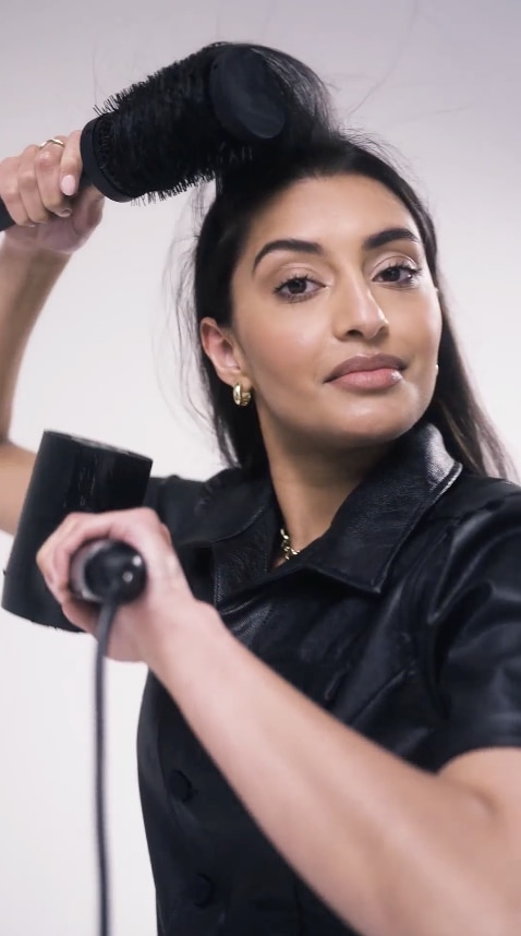 A model with part of her blonde hair up in hair clips and a stylist applying mousse to it