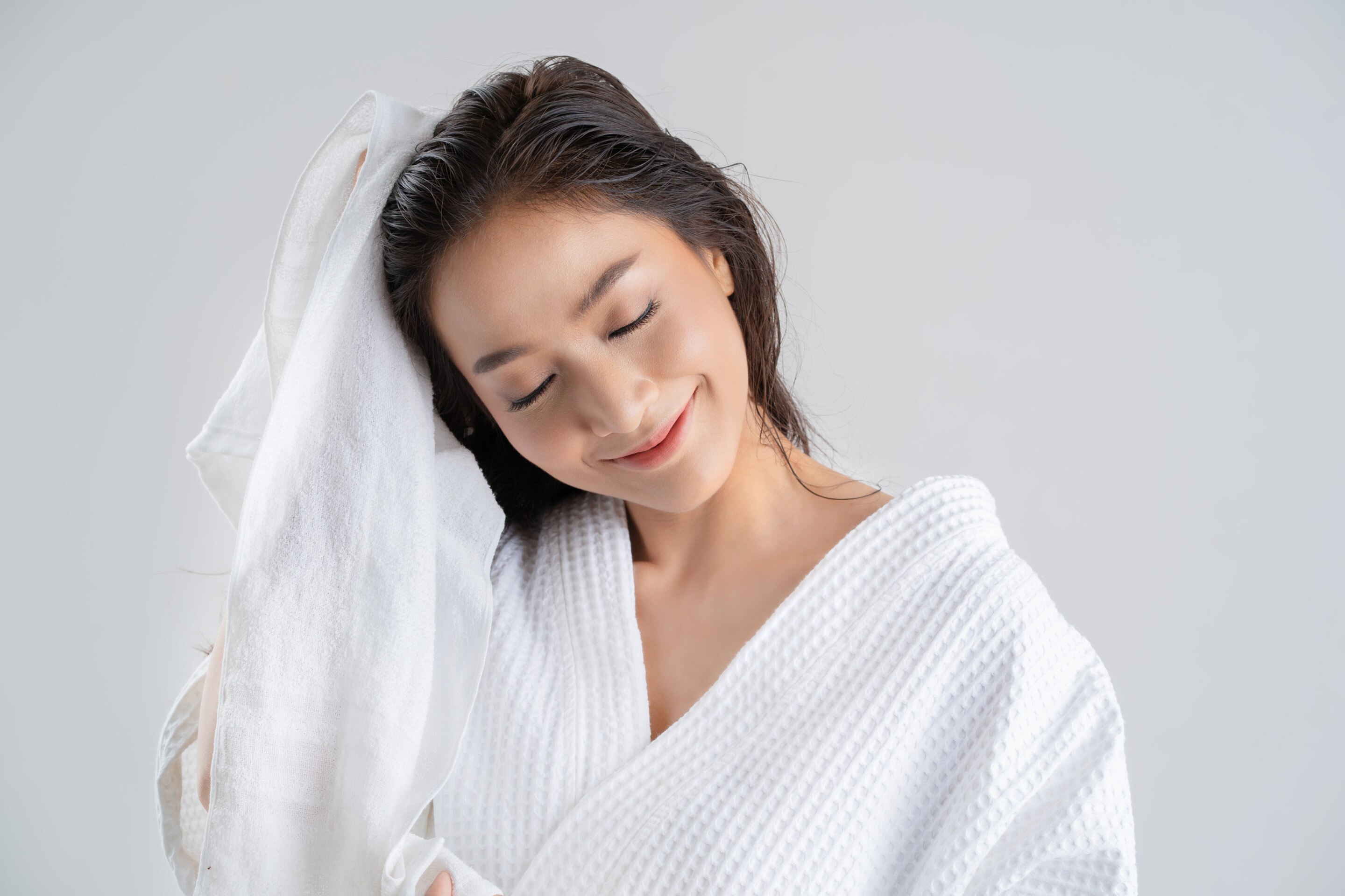 A beautiful Asian woman in a white robe and rubbing her hair with a towel