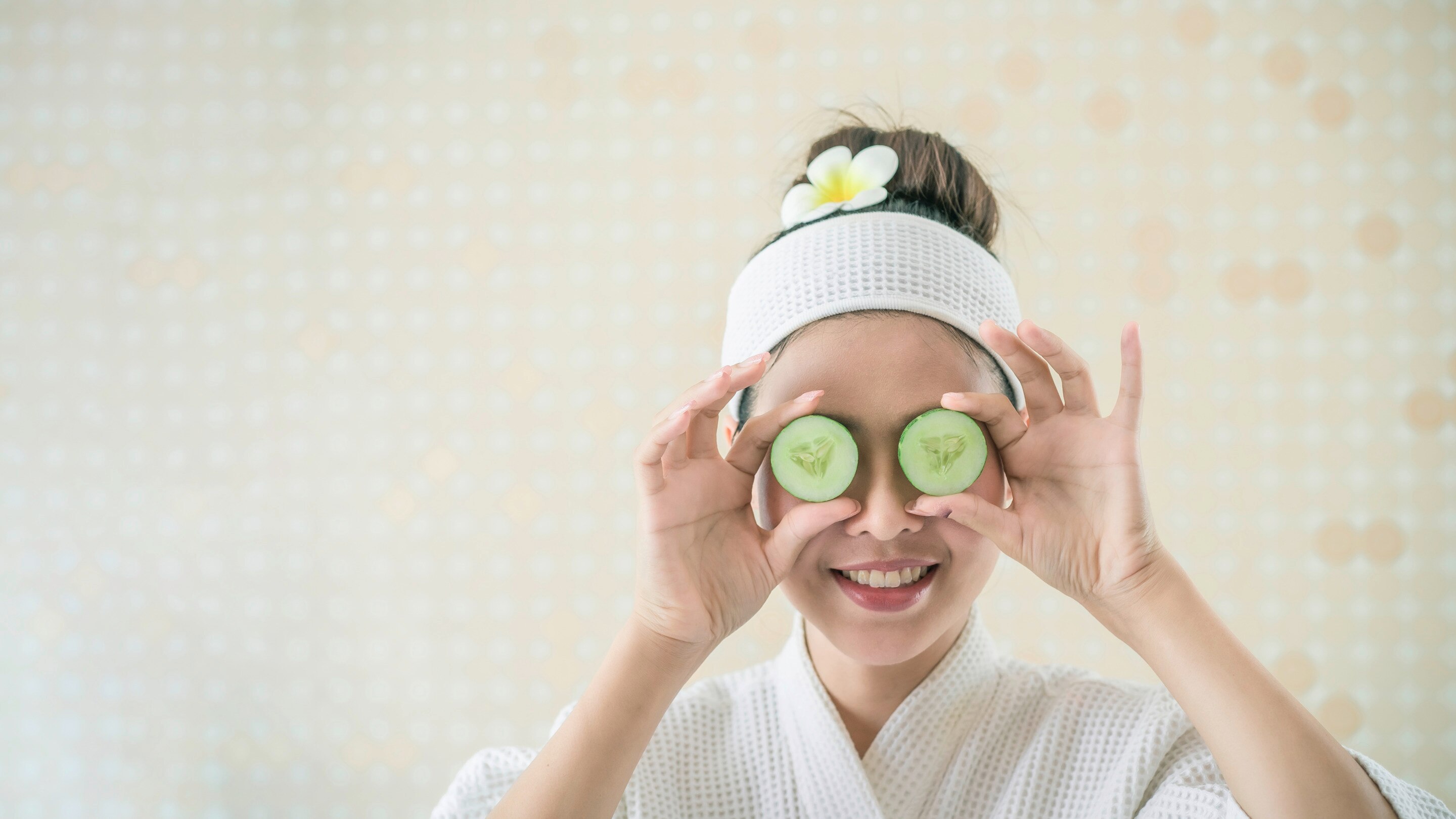 Asian woman holding cucumbers over eyes