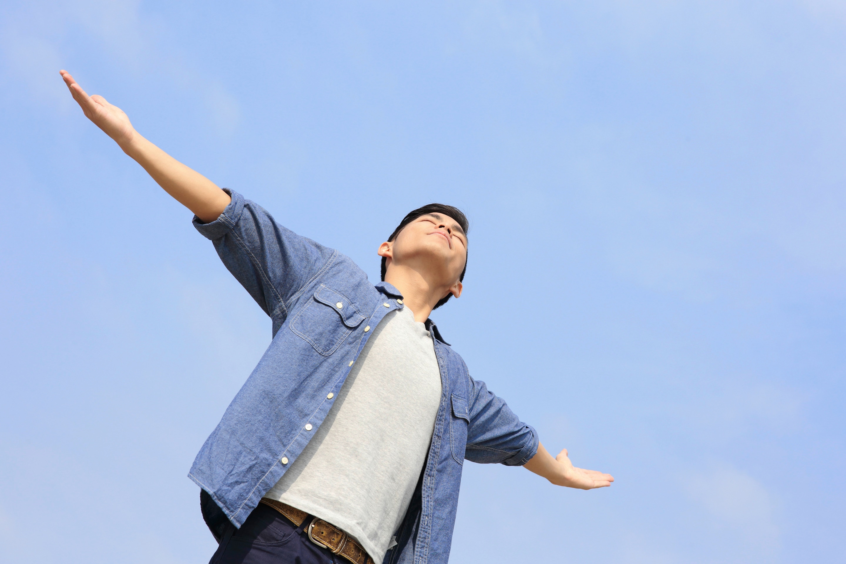 Asian man with arms spread against blue sky