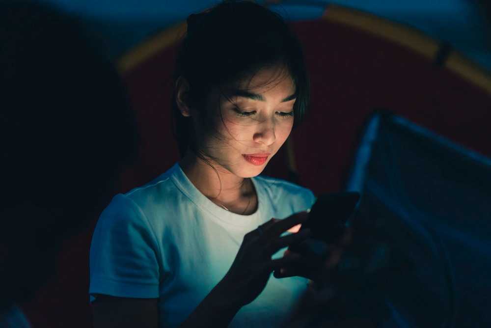 Asian woman in white shirt using phone in the dark.