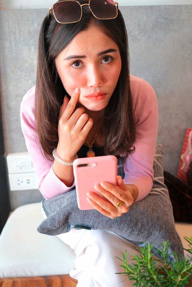 Asian woman in pink holding pink phone while touching cheek.