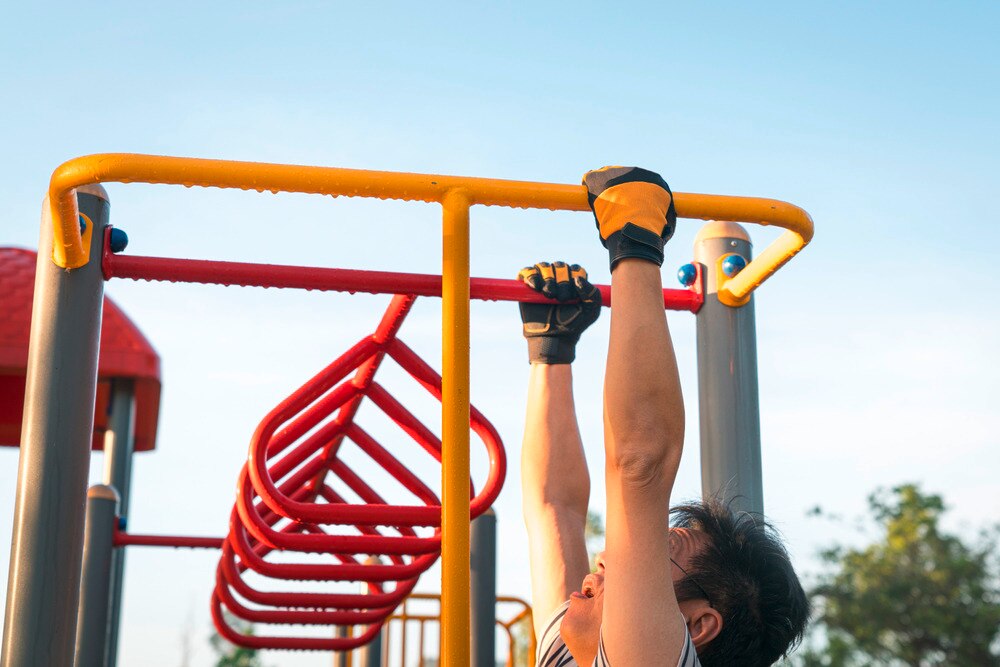 Asian man holding on to monkey bars outdoors.