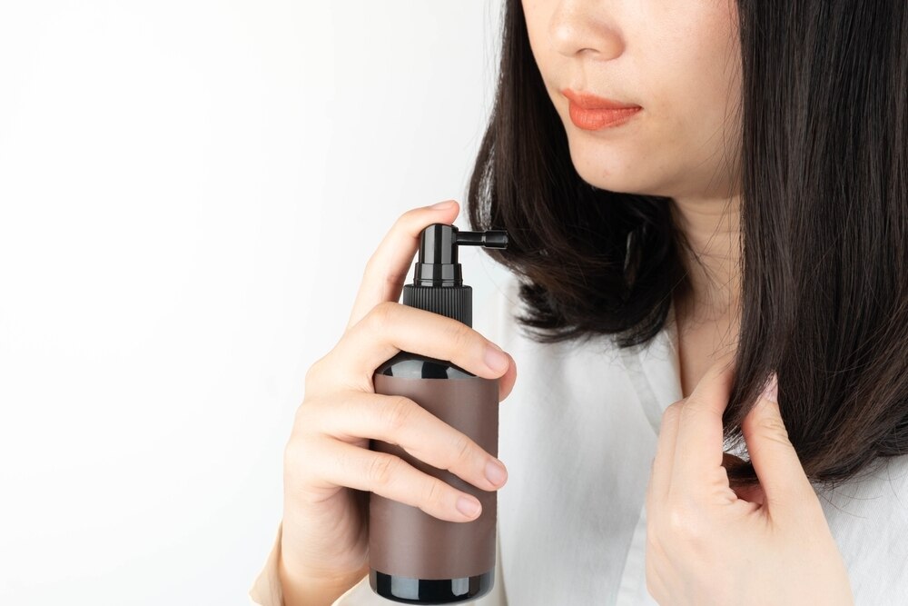 Closeup of an Asian woman applying hair product. 