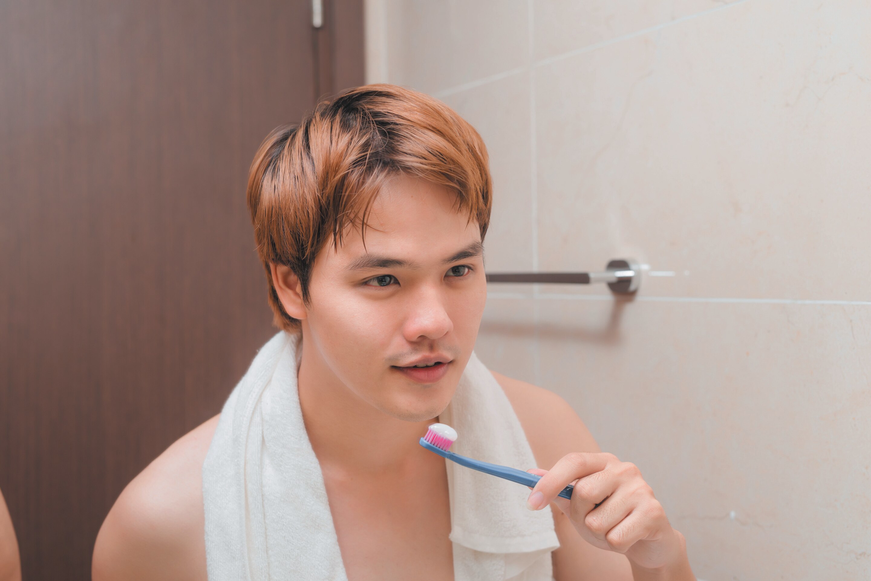 Asian man with highlighted hair brushing teeth