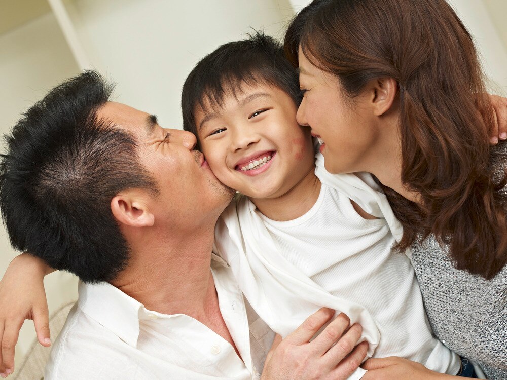 Asian couple kissing their child on the cheek