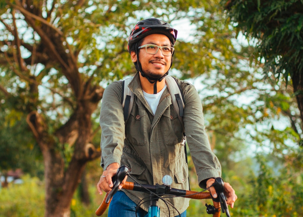 Asian man with a helmet and backpack biking outdoors. 