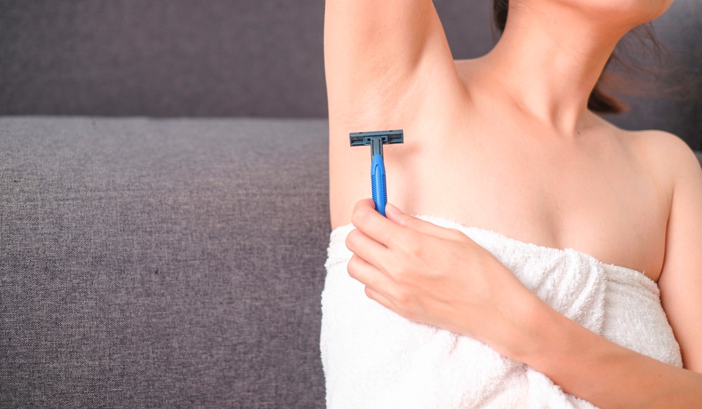 Closeup of a woman in a towel shaving her armpit.