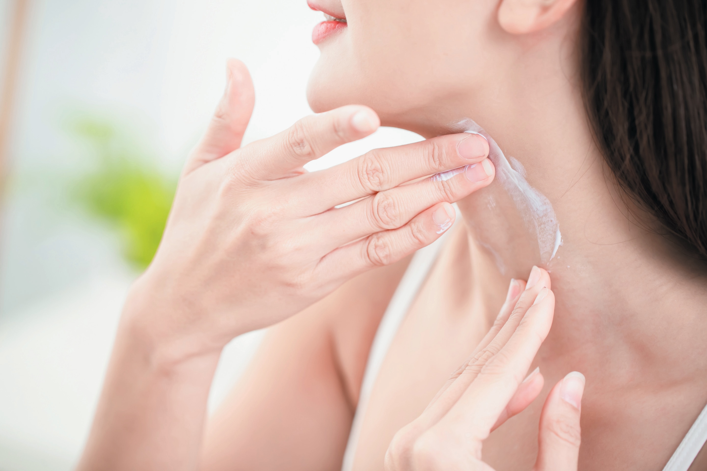 Asian woman applying cream on her neck