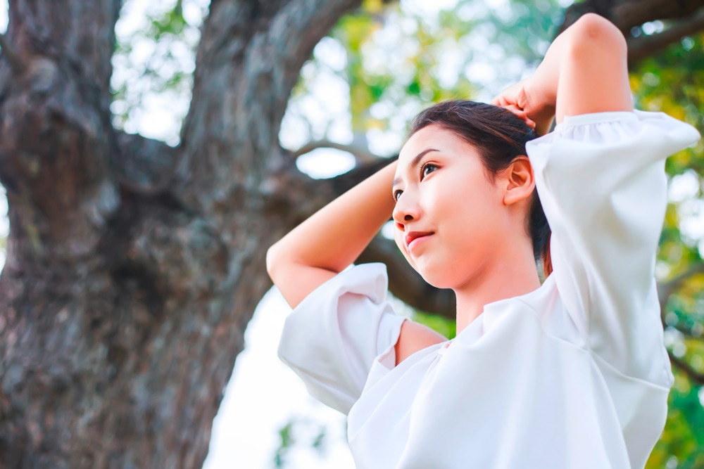 Asian woman in a white top tying her hair.