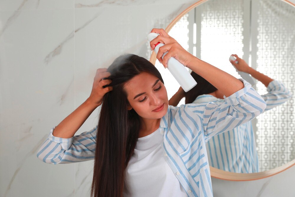 Woman applying dry shampoo to her hair roots.