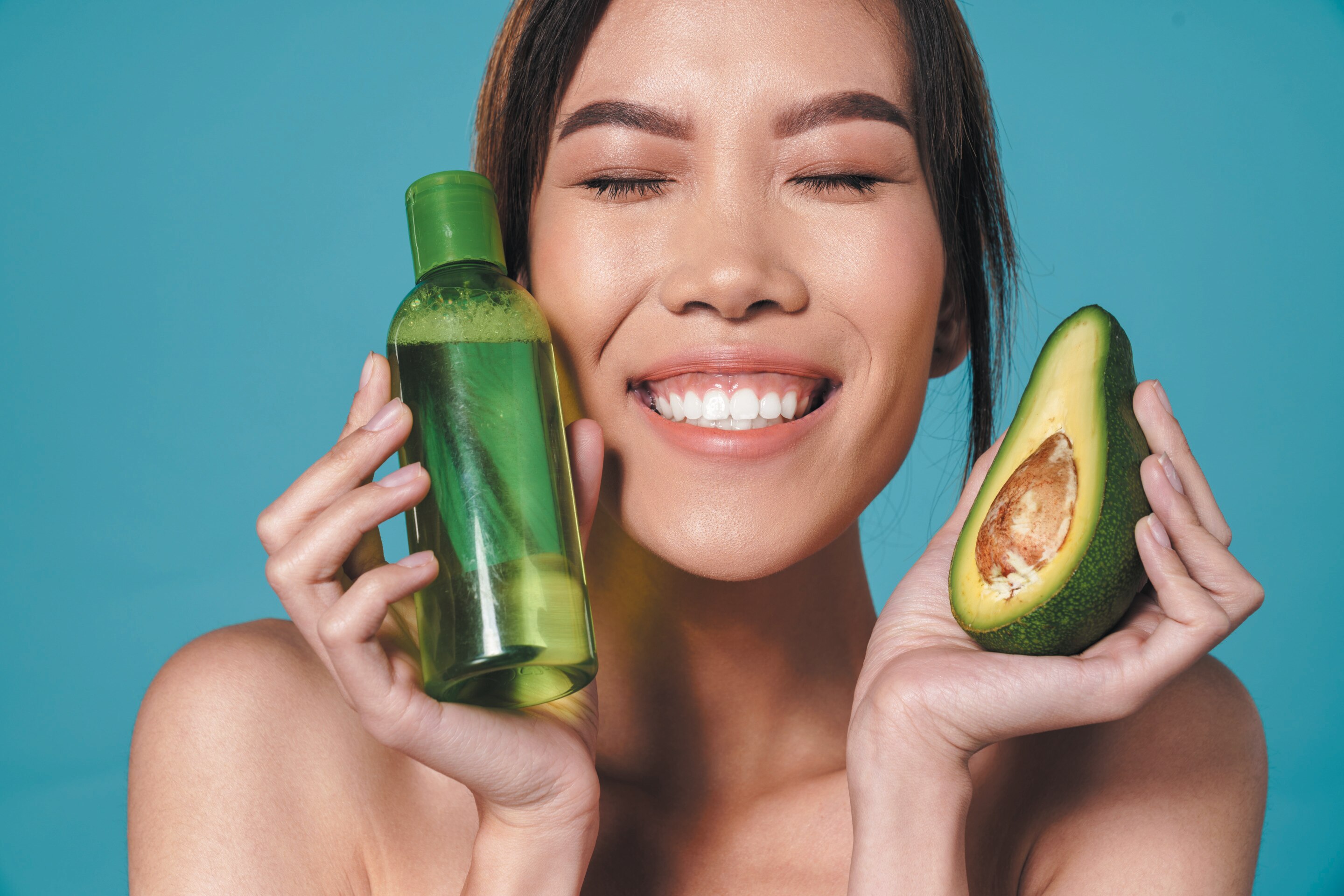Asian woman holding avocado and a bottle of skincare