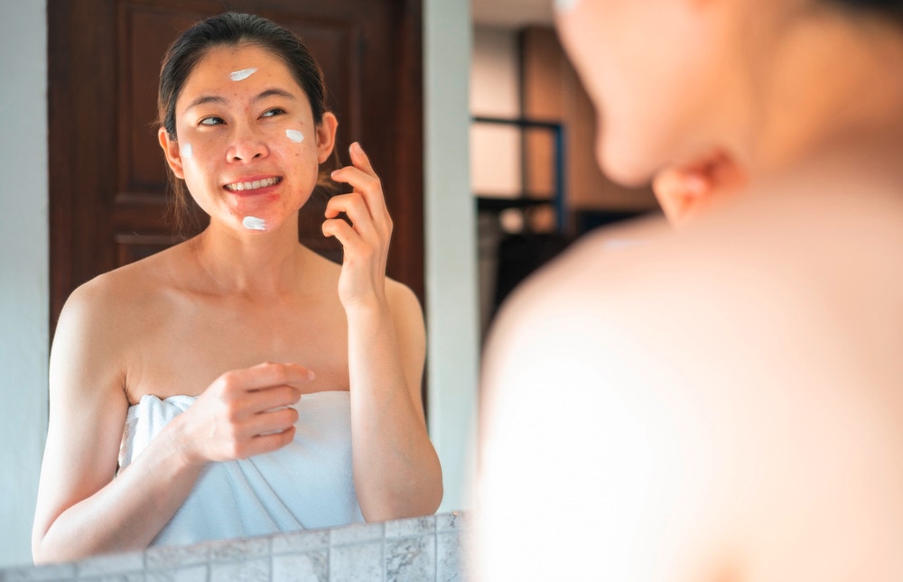 Woman applying sunscreen on her face while standing in front of the mirror.