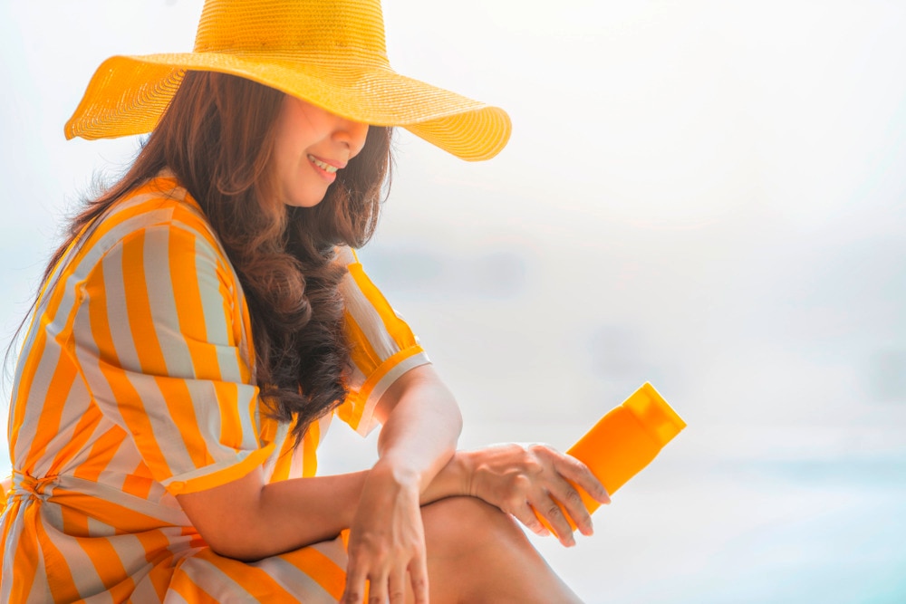 A portrait with yellow sun hat holding a sunscreen bottle.