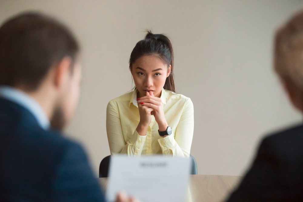 Asian woman in yellow shirt looking nervous in front of male bosses.