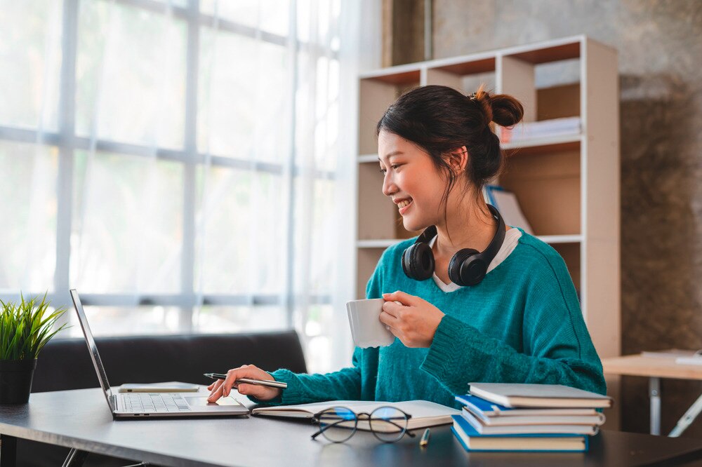 Woman doing research on her laptop while holding a cup of beverage.