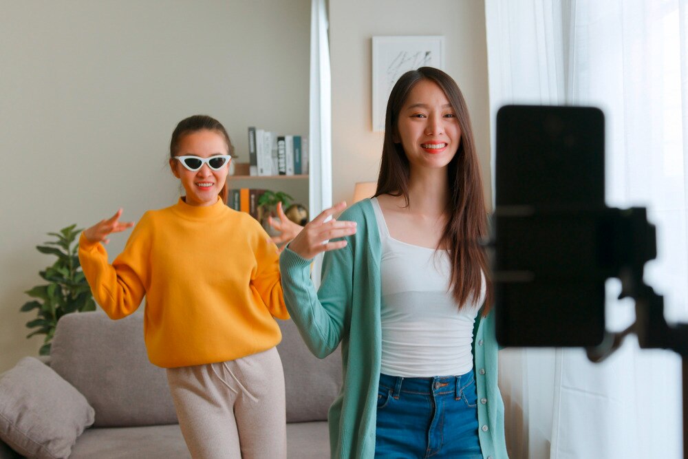 Pair of Asian women dancing in front of cellphone.