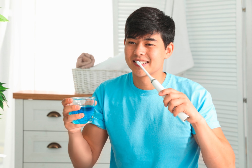 Asian man in blue shirt holding a toothbrush and mouthwash