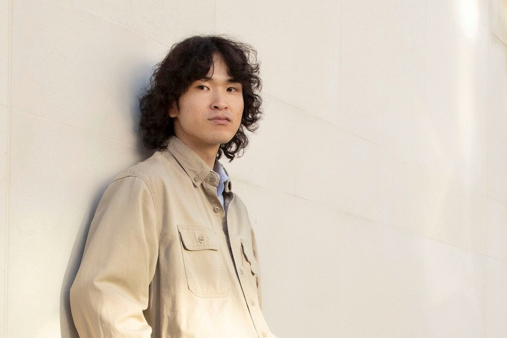 Man with permed hair leaning against the wall.