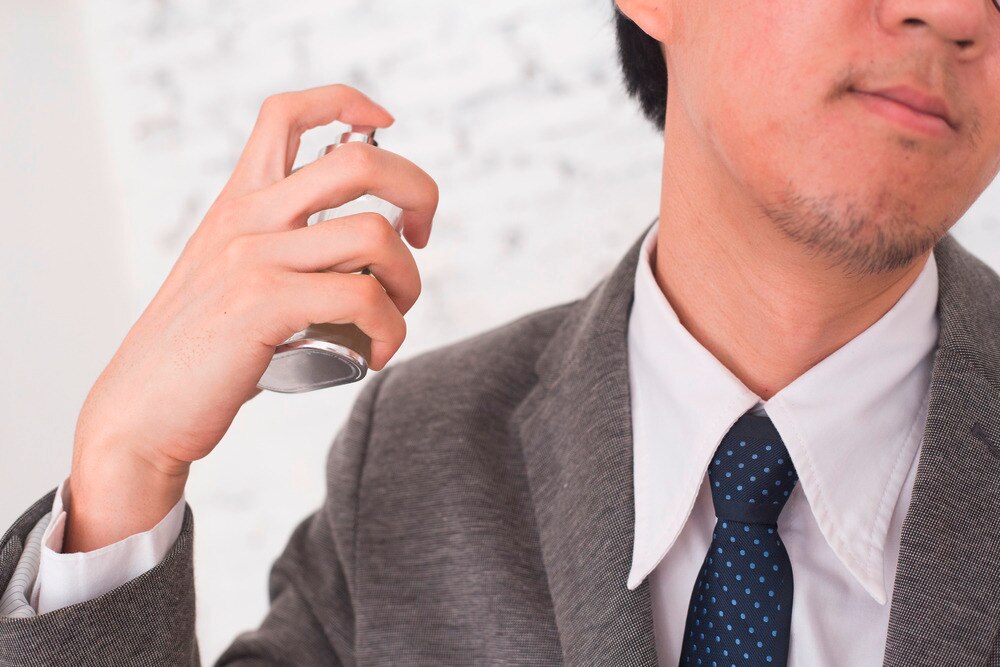 Closeup of an Asian businessman spraying on some cologne.