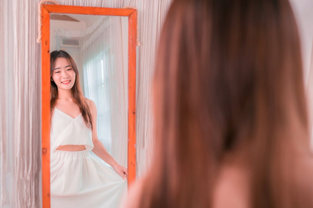 Asian woman looking at her outfit in the mirror.