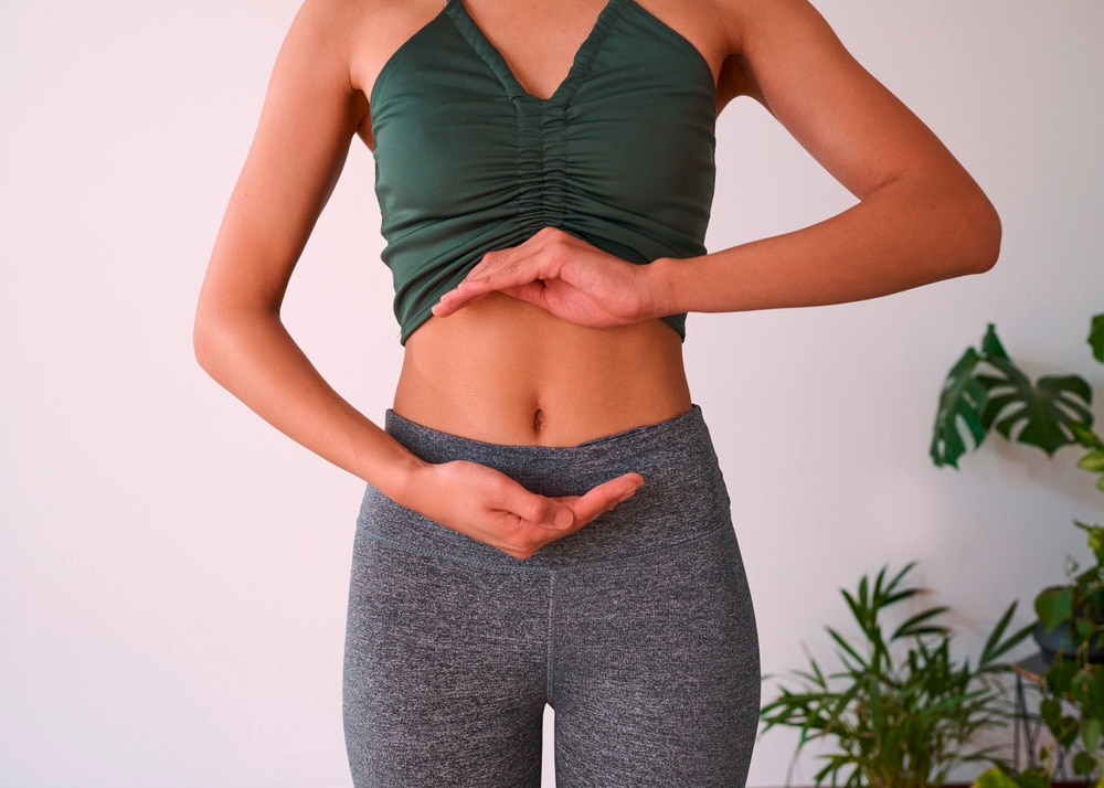 หญิงสาว ผมหยิก ยืน กลางแจ้ง  วางมือรูปสามเหลี่ยม ทาบบนผิวหน้าท้อง