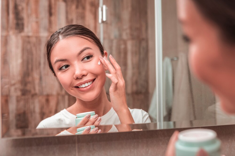 A portrait of woman applying cream onto her face.