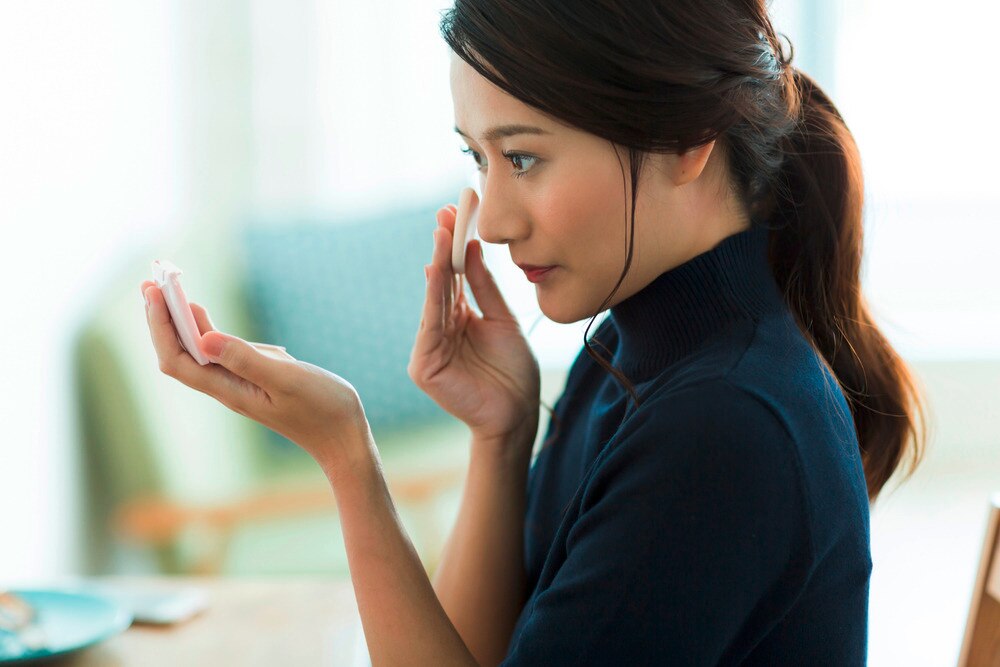 A portrait of woman applying foundation with a sponge.
