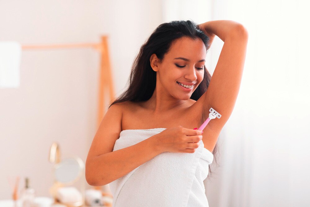 Woman dry shaving her underarms with pink razor.