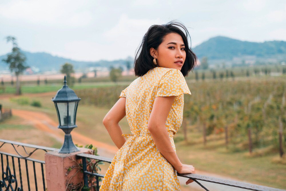 A portrait of woman in yellow sundress standing on a balcony.