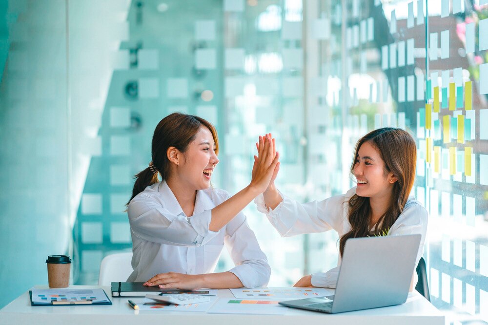 Two Asian women high-fiving at work.