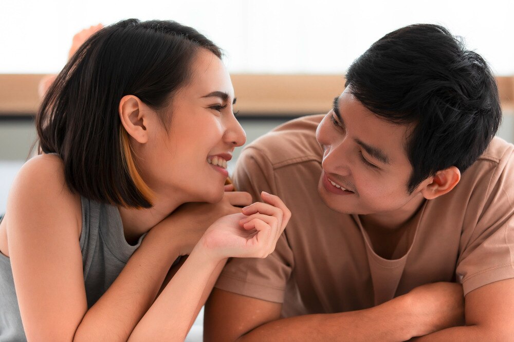 Asian couple lying on a bed, looking at each other fondly