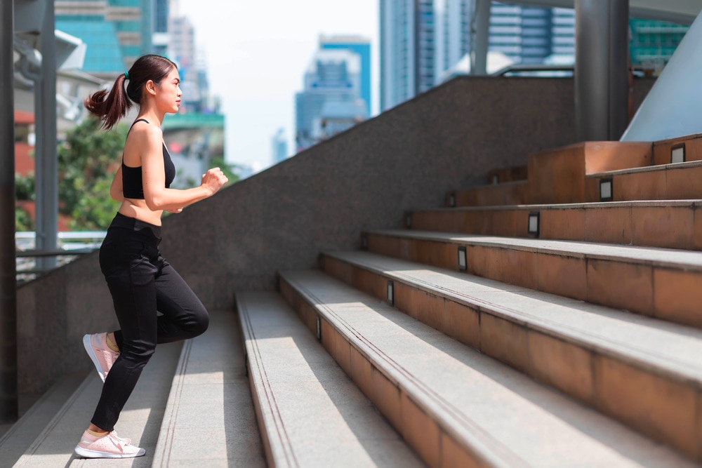 Asian woman running up a flight of stairs in pants and crop top.