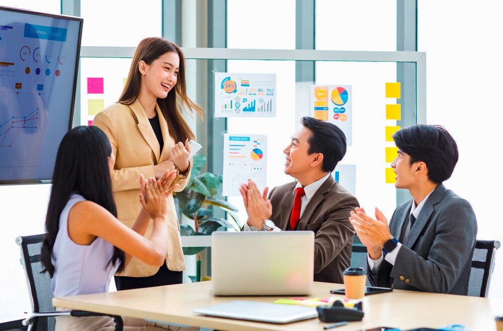 Woman giving presentation and getting praised by her colleagues.