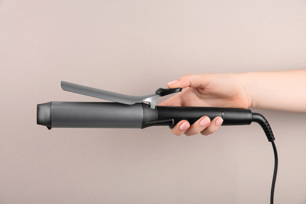 A hand holding a curling wand with clamp.