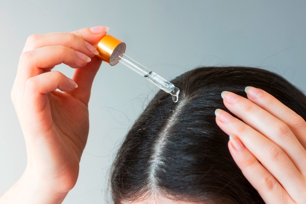 Woman applying hair oil onto her scalp.