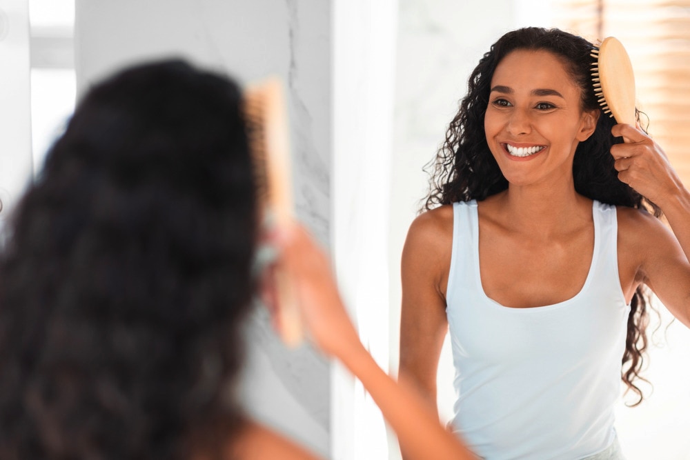 Woman brushing her curly hair in front of a mirror.