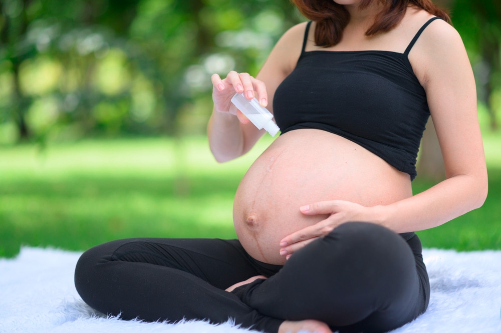 Pregnant woman applying body oil onto her baby bump.