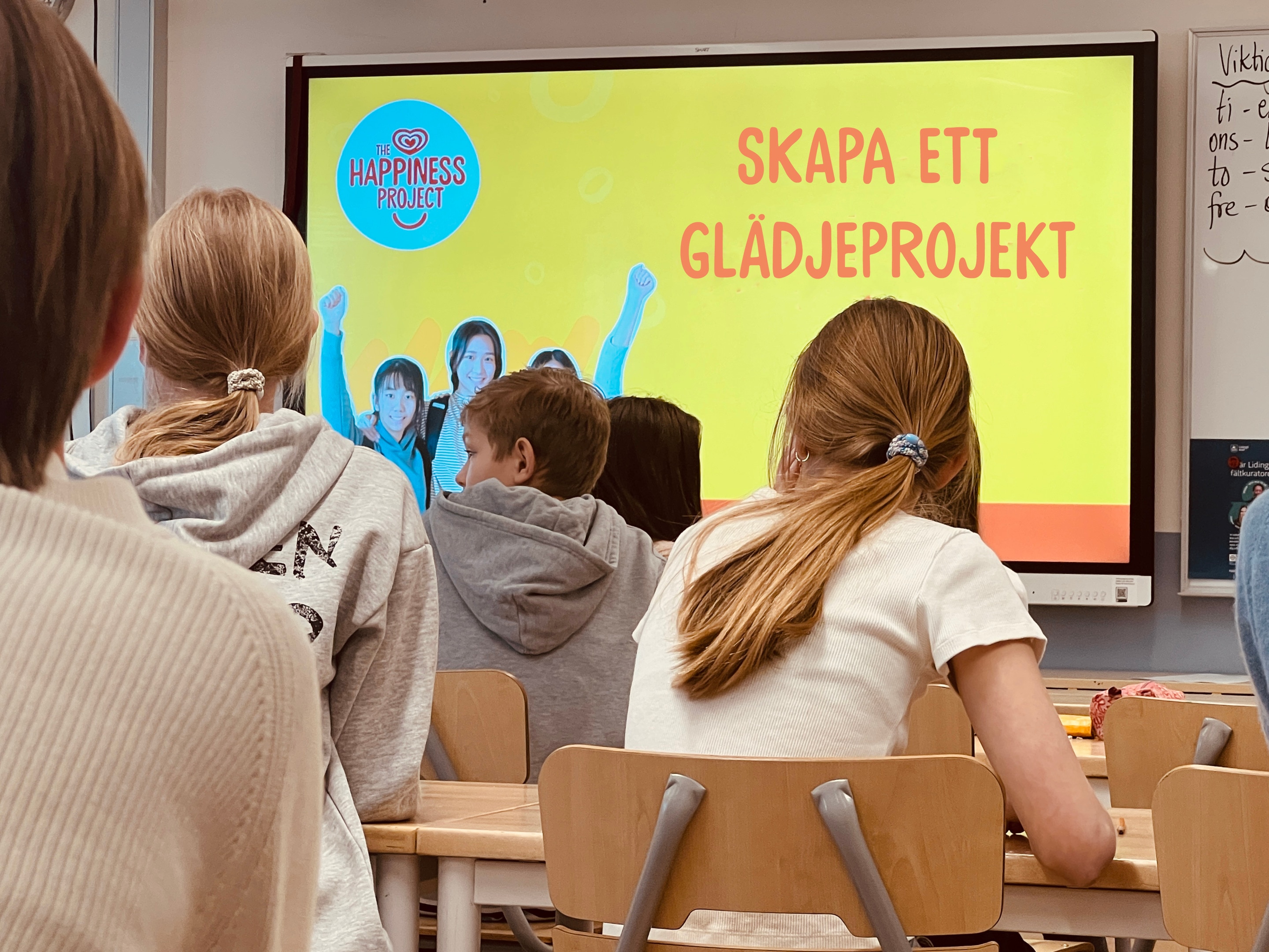 A backshot of students in a classroom with a happiness lesson projected in front a backshot of students in a classroom with a happiness lesson projected in front