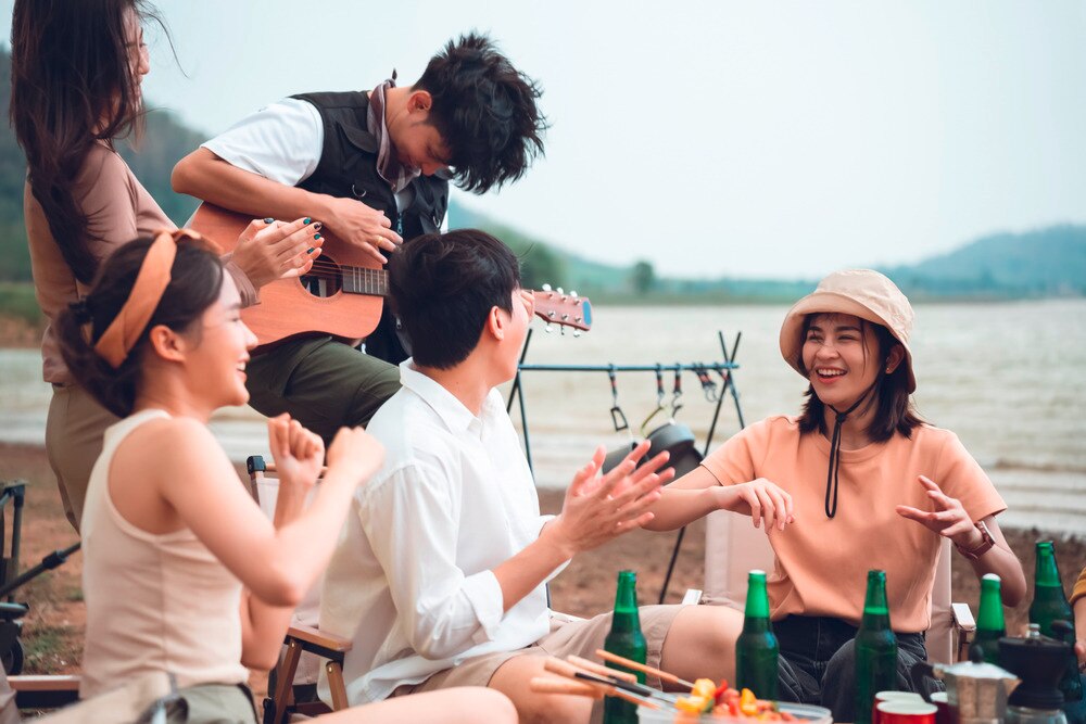 Asian friends hanging out outdoors with drinks and guitar.