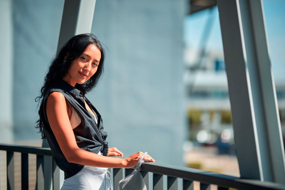 Woman with black top and white pants posing in a corridor.
