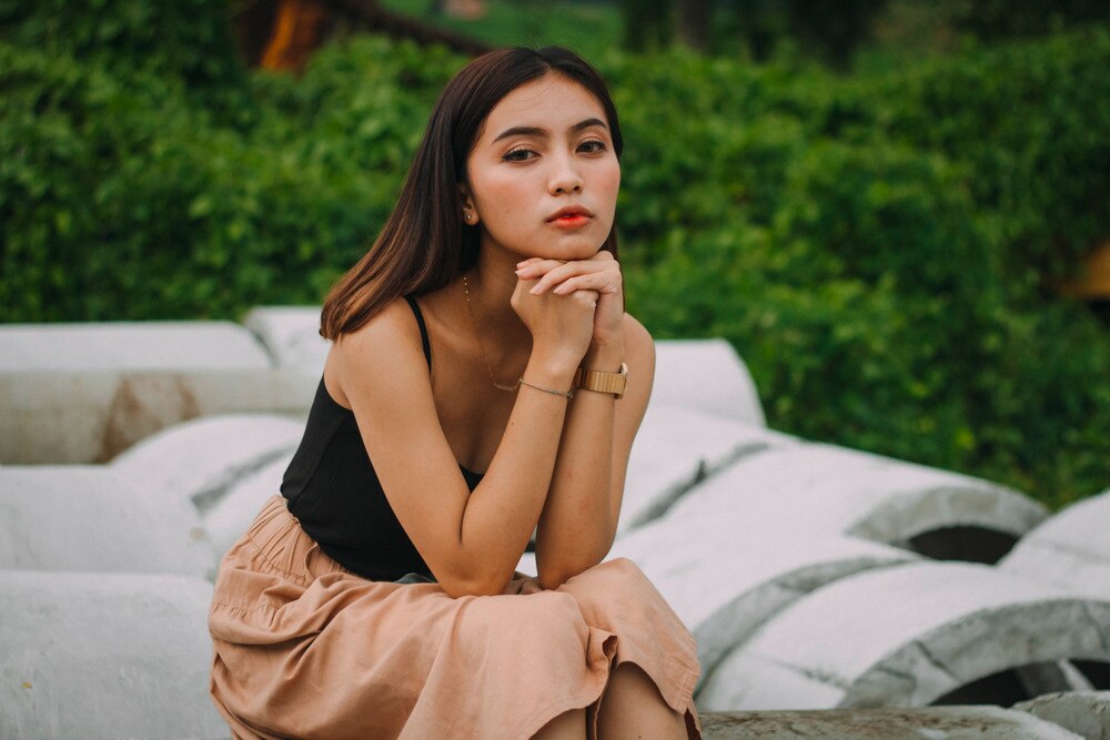  A woman sitting on a lounge chair with her hands clasped under her chin.