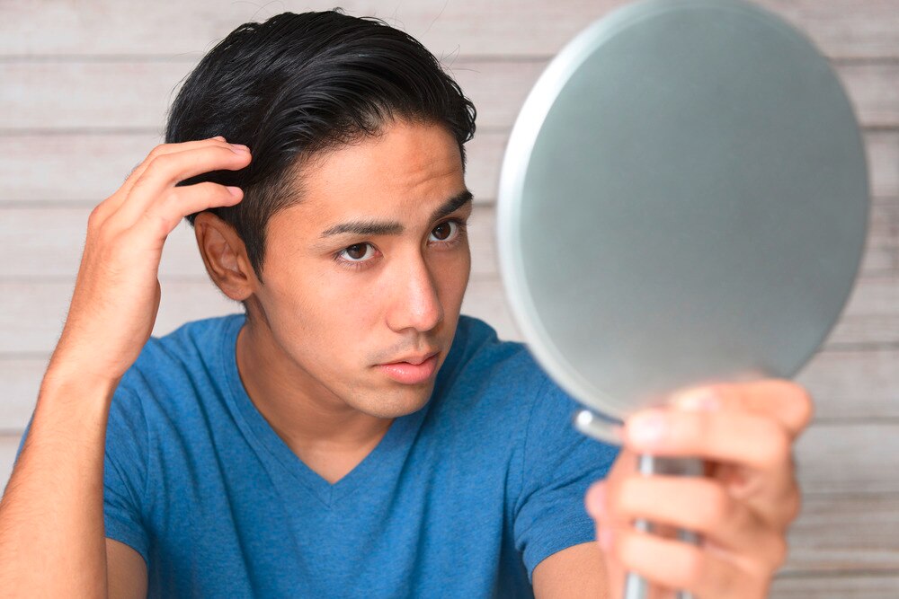 Man checking his yellow dandruff with a handheld mirror.